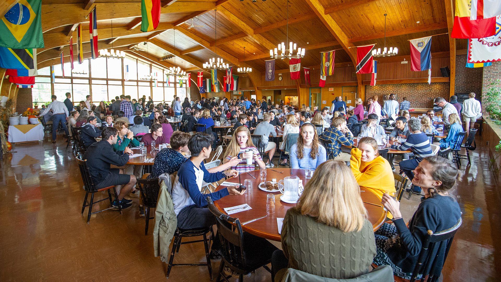 Head of School Search for Vermont Academy conducted by Educators Collaborative. Photo shows a cafeteria full of students with colorful flags from around the world hanging above.